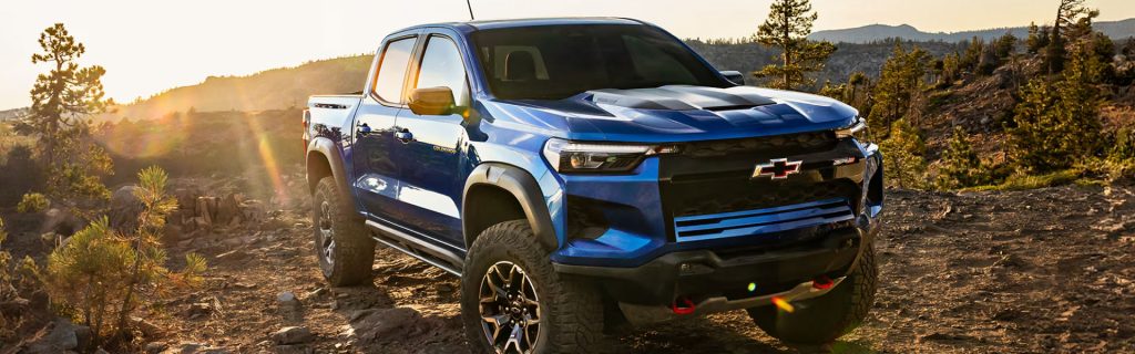 Blue Chevrolet Colorado parked on a rocky trail at sunset.