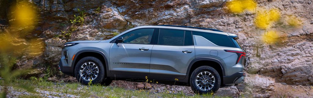 Silver Chevy Traverse parked in front of a rocky cliff.