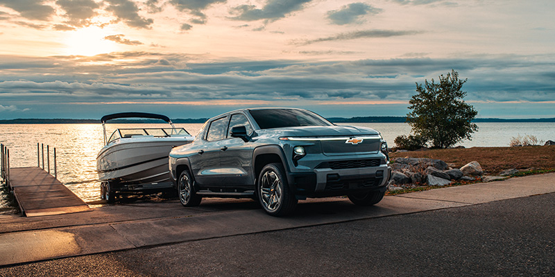 Chevrolet Silverado EV towing a boat at a lake during sunset.