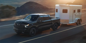 Black Chevrolet Silverado from Valley Stream, NY towing a camper on the open road.