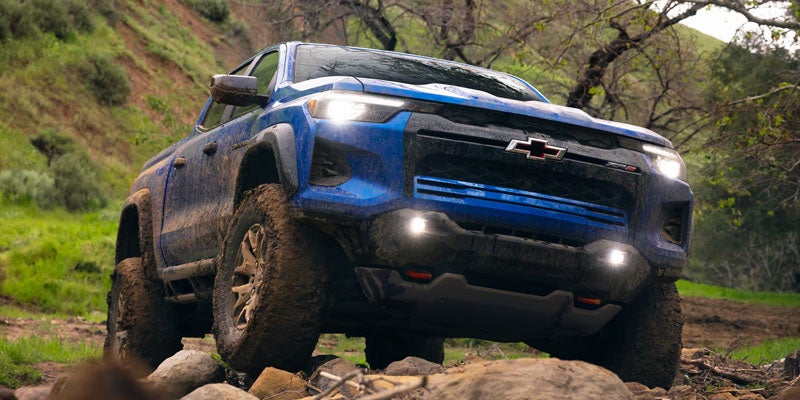 A blue 2026 Chevy Colorado driving through rocky natural terrain.