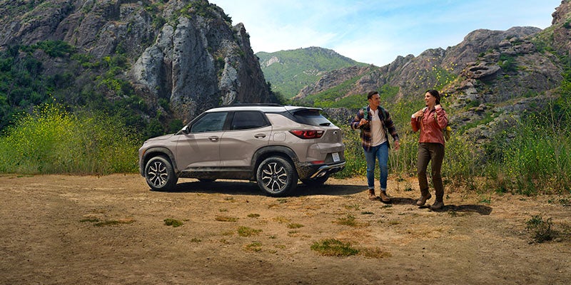 Gray Chevrolet Trailblazer SUV parked near a mountain trail with two people exploring the outdoors